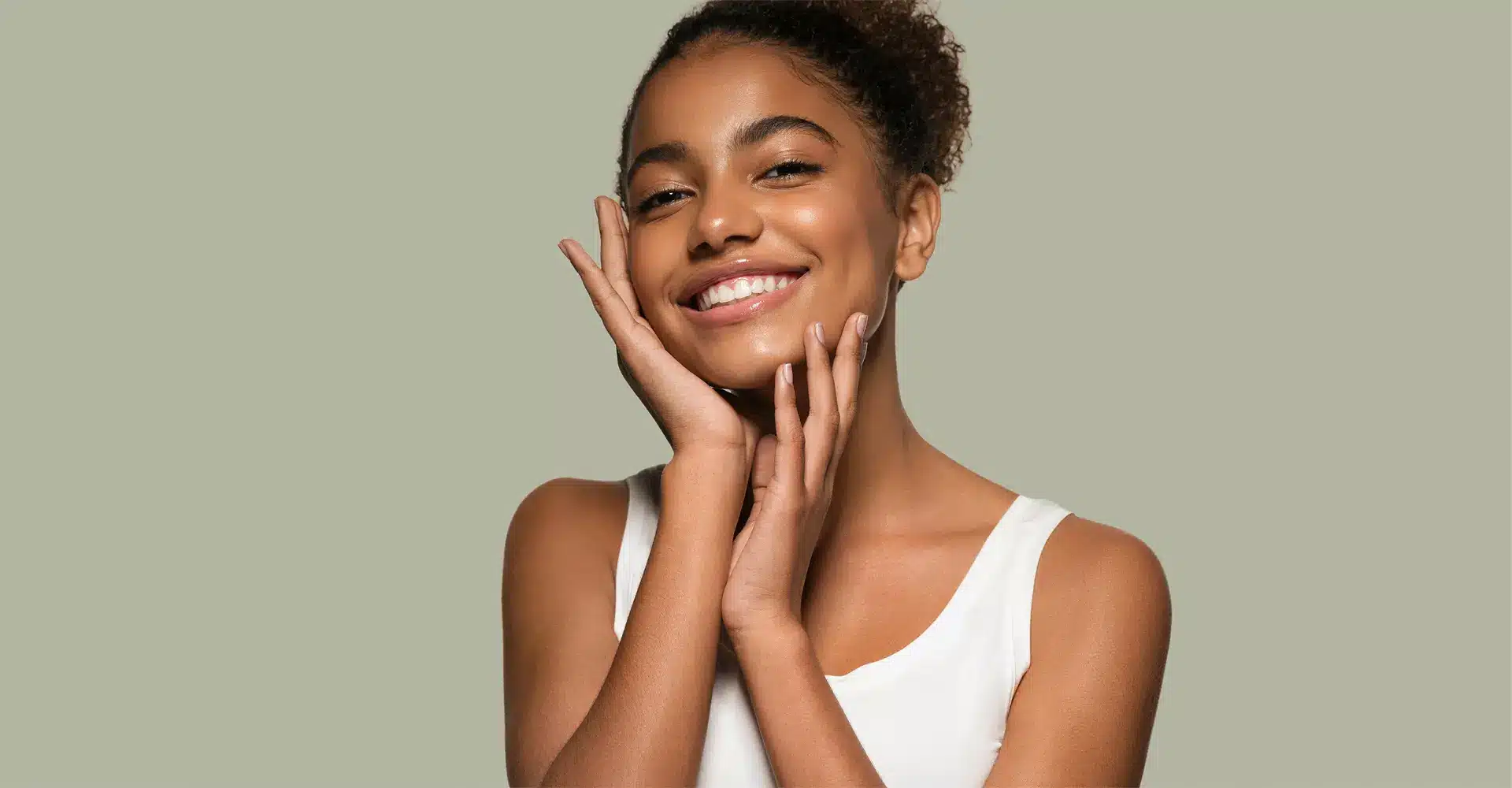 a young woman with curly hair smiles brightly gently touching her face with both hands she is wearing a white sleeveless top and is set against a plain light green background her radiant skin hints at the effectiveness of picoway resolve treatments